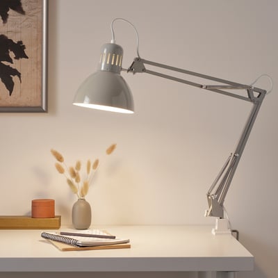 Grey TERTIAL desk lamp with flexible arm on white desk near vase and books.