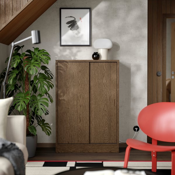 Modern room TONSTAD wooden cabinet with sliding doors, a large green plant, and a red chair. Abstract art hangs above.
