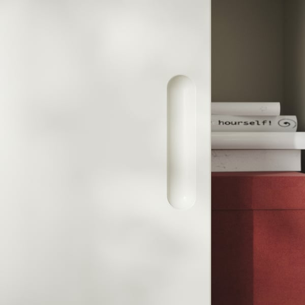 White modern cabinet with cylindrical handle, red interior, displaying neatly stacked books.