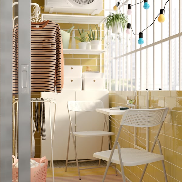 Bright room with small white TORPARÖ dining set by yellow-tiled wall. Colourful string lights hang from the ceiling, and a striped shirt hangs nearby.