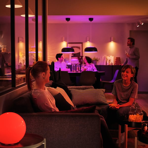 Two people on sofa, one with drink, other smiling. Bar area in background, soft TRÅDFRI lighting.