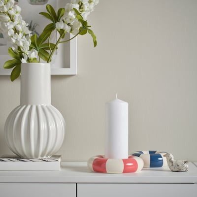 A TRÄDSTAM white candle holder like a swim ring sits small on a shelf, accompanied by a larger white candle and decorative objects.