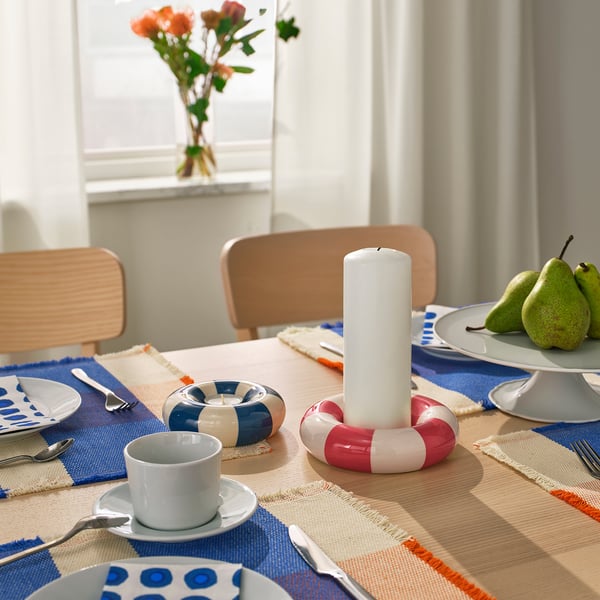 Dining table with blue placemats, white plates, silver cutlery, candle holders, flowers.