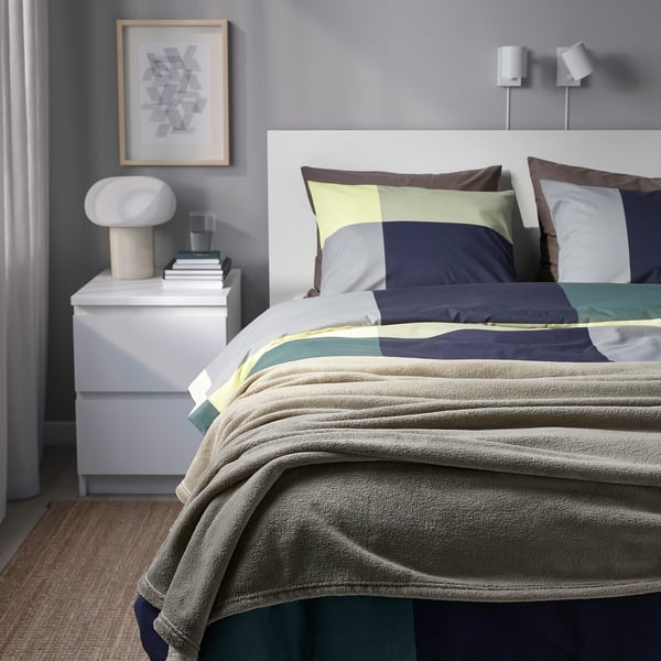 Cosy bedroom with TRATTVIVA bed, neutral colours, striped blanket, colourful pillows, bedside table with lamp and books.