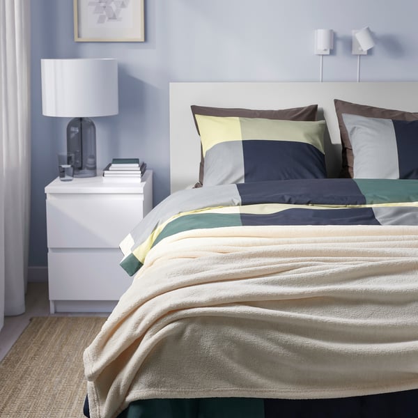 Modern bedroom with striped bedspread on large bed, white headboard, recycled polyester, various cushions.