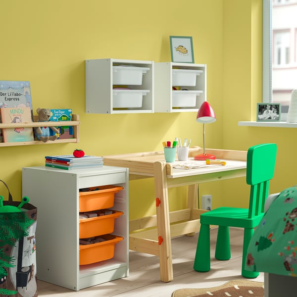 Kids room with TROFAST white storage, orange bins, green chair. Bright, organised space.