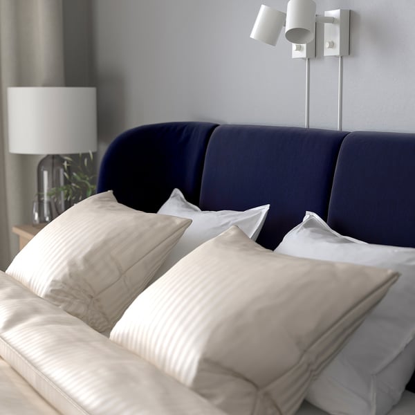Bed with dark headboard, white pillows & lamp on bedside table.