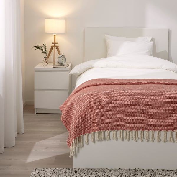 Cosy bedroom with blush pink throw on white bed, wooden headboard, and bedside lamp.