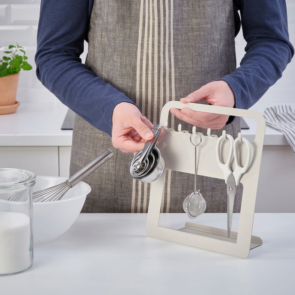 Person in apron holding measuring cups on white utensil holder.