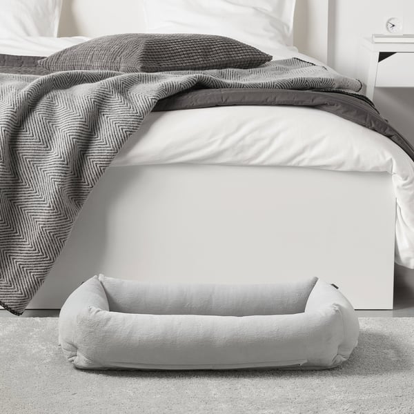 A soft pet bed near a bed, with raised sides for comfort and support, ideal for dogs up to 20 kg.