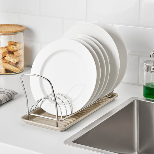 Silver metal dish drainer holds white dishes near sink; practical for small spaces.