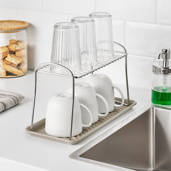 Kitchen scene with a stainless steel, two-tier dish drainer holding white and clear cups. Its positioned near a sink.