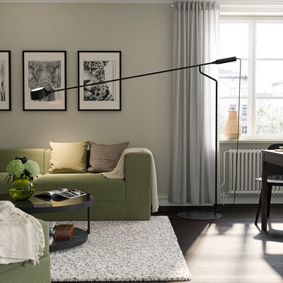Modern living room: green sofa, photos, VÅGHÖJD lamp, white rug, coffee table, window with curtains.