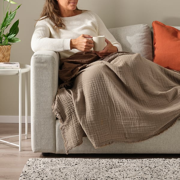 Person relaxes on couch with VALLKRASSING throw, enjoying cosy setup.