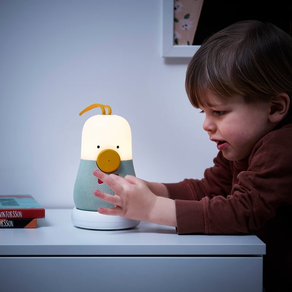 Child pressing yellow button on VAPPEBY speaker lamp, which plays music and changes light.