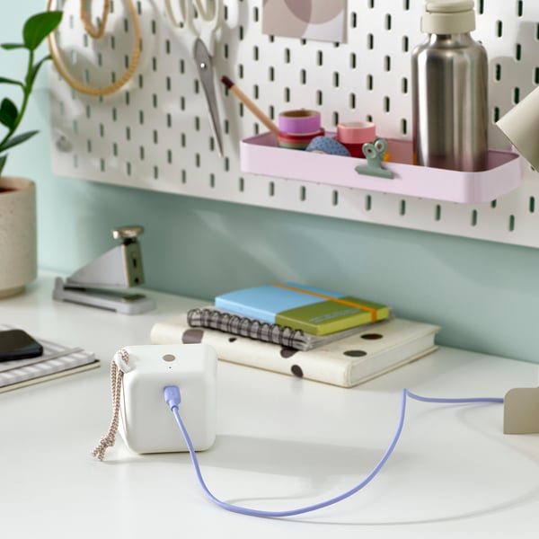 A neatly organised desk with a portable bluetooth speaker, colourful notebooks, and stationery items on a pegboard.