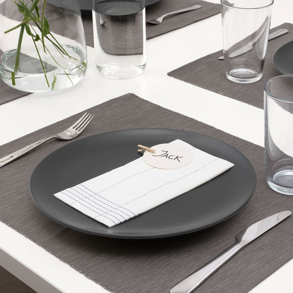 Elegant table setting with grey plate, folded white napkin, simple name tag, and modern cutlery, ready for dining.