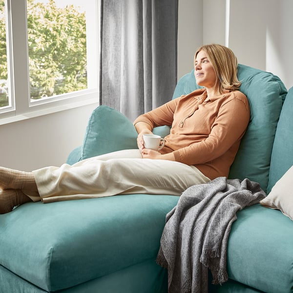 Person relaxing on blue VINLIDEN sofa, holding coffee cup, with large cushions and soft fabric.