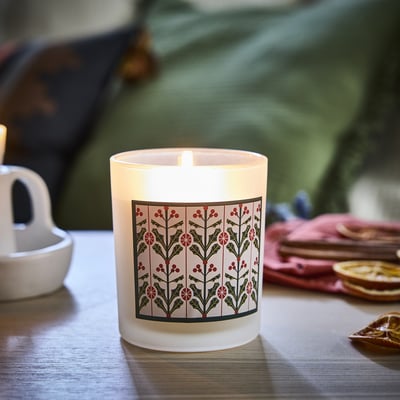 Small VINTERFINT candle in glass, lit; white with green, red holly design.