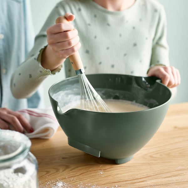 Person whisking batter in large green mixing bowl with handle on wooden countertop.