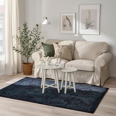 Beige sofa, small tables, blue rug, green cushions, wall art.