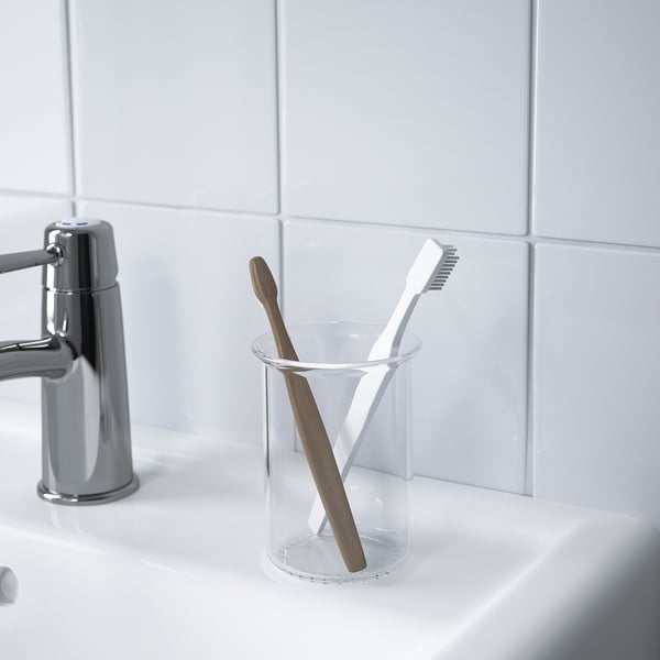 Two toothbrushes in a clear glass holder, placed on a white sink near a chrome tap.