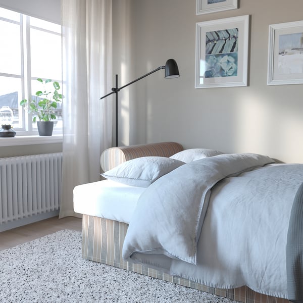 Cosy bedroom with white bedding, wooden bench, plant, and floor lamp. VRETSTORP sofa converts to bed effortlessly for guest comfort.
