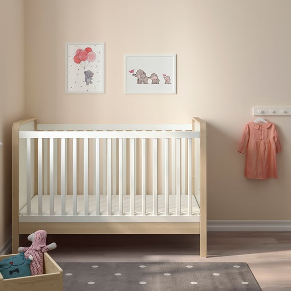 Wooden crib with nursery decor, elephant pictures, peach dress, toy basket on rug