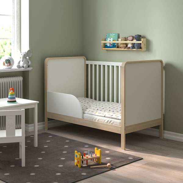 Childs room with green walls, white cot, changing table, toy shelf, and train set.