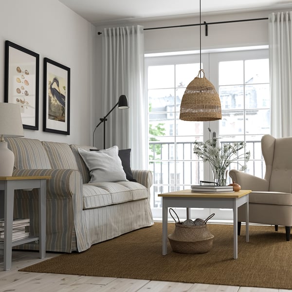 Modern living room with side table, striped sofa, beige chairs, and wooden elements near a window with sheer curtains.