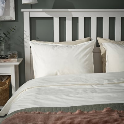 ÄNGSLILJA white cotton pillowcases on bed, with wooden headboard, lamp, and bedside table.