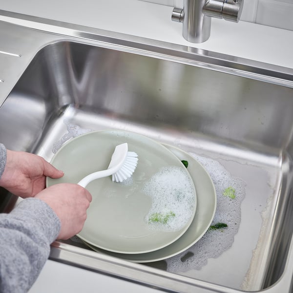 A person cleaning a plate with a brush in a sink.