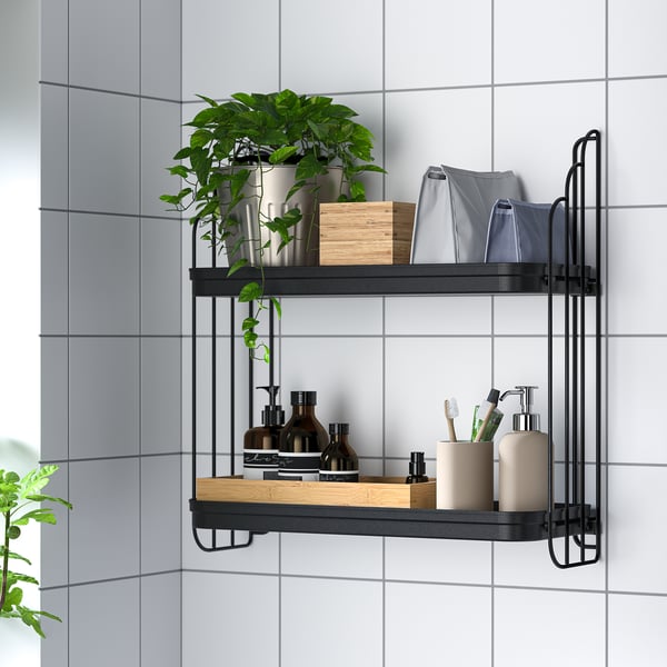 Wall-mounted shelf with two tiers storing bathroom items: bottles, toothbrushes, towels, and a plant in a tiled room.