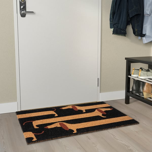 Playful dachshund doormat at entryway with shoe rack and jackets.