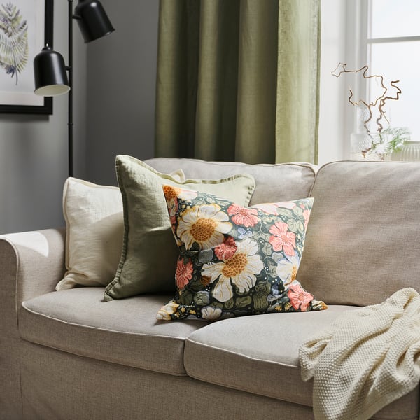 ARENBOK pillow on beige couch with floral design.