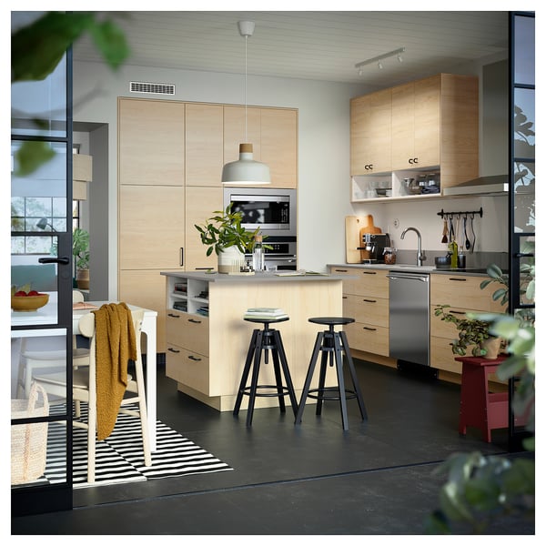 Modern kitchen with light wood cabinets, black countertop appliances, and black stools.