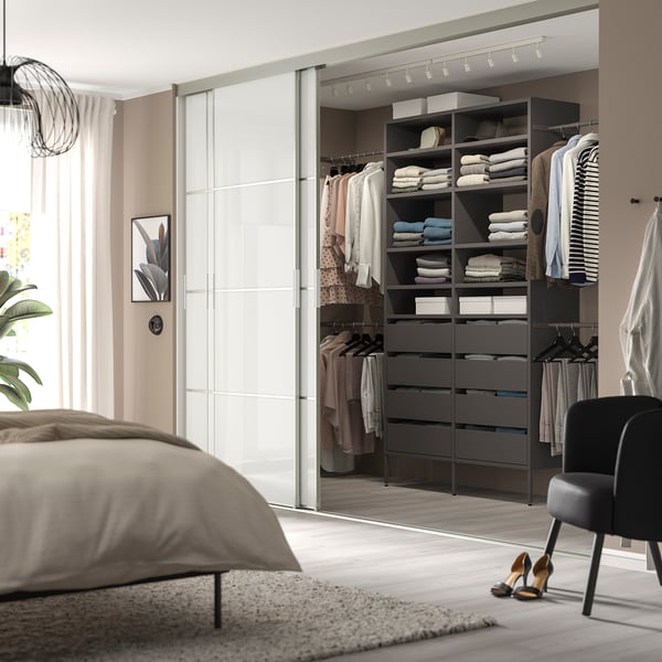Modern bedroom with AURDAL closet, grey storage, neatly organised clothes, large bed, black chair, rug, and track lighting.