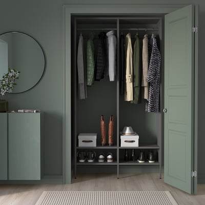 Modern closet with green AURDAL shelves and hangers. Shoes organised, clothes hanging, round mirror and wooden floor.