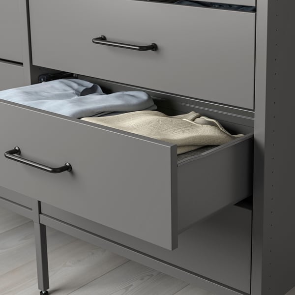 Open grey drawer of AURDAL wardrobe displaying folded light-colored clothes on shelf.