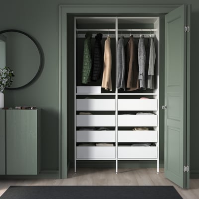 White closet system with drawers, hangers, against green wall, mirror, plant, open door.