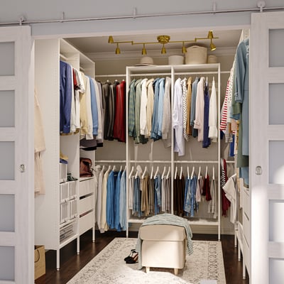 White closet system with clothes, shelves, drawers, and ottoman.