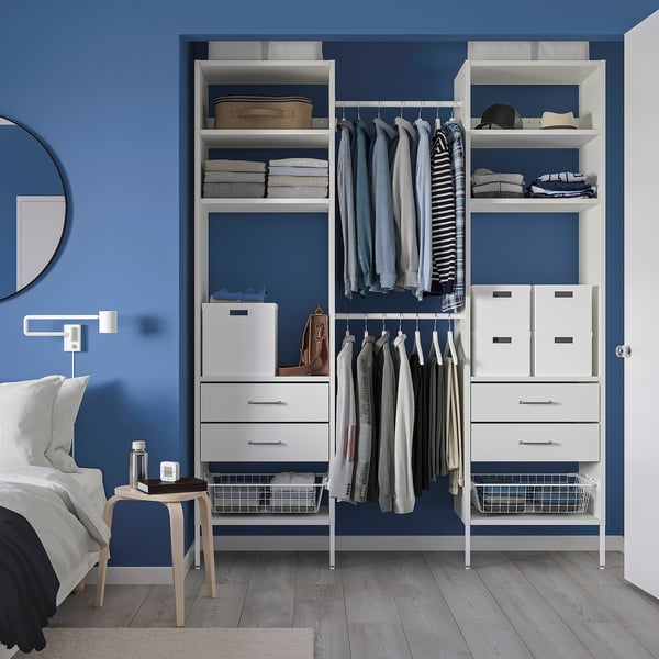 Blue closet with white storage, shelves, drawers, and hanging space. Surrounds a bed with a grey side table.
