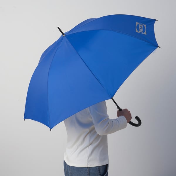 Person holding large blue IKEA umbrella, open and ready for rain.