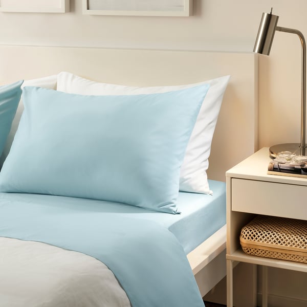 Blue sheets on bed, white pillow, lamp, basket.