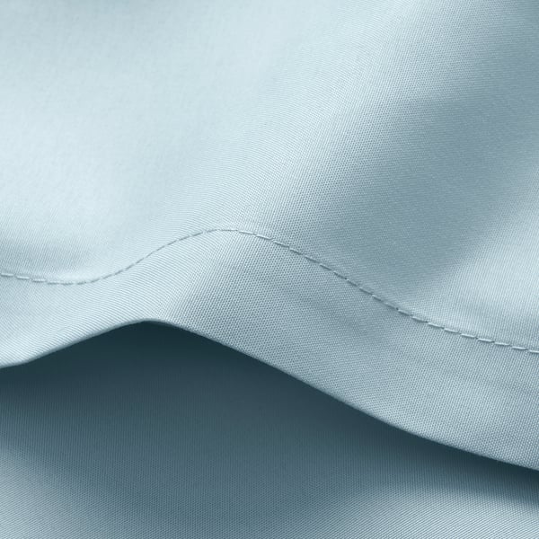 A close-up of soft, light-colored sheets, showcasing the detailed stitching along the edges, highlighting their quality and comfort.