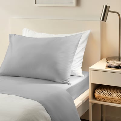 Grey bed sheet set on mattress up to 25 cm. Soft, recycled polyester. Beside table with lamp and basket.