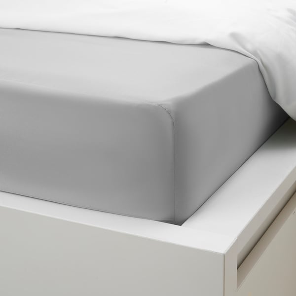 Bed with grey fitted sheet on white frame, displaying elastic edges for secure fit.