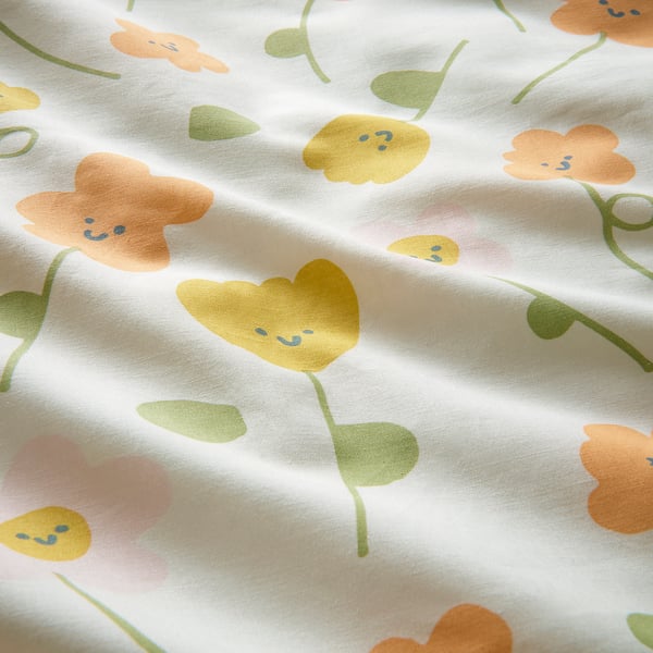 Floral fabric close-up, soft, light colours, yellow, orange flowers, green leaves, smiley faces.