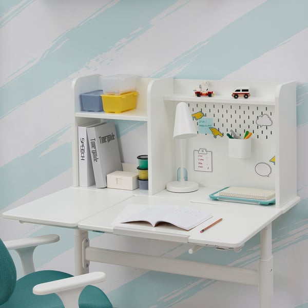 A childs adjustable study desk with tiltable top, shelf, and pegboard for storage, against a blue-painted wall.