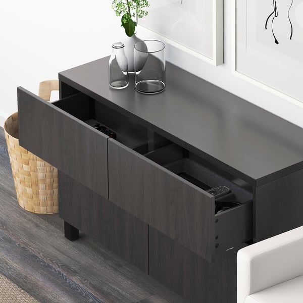 Dark wooden drawer unit with visible compartments holding remote controls and small items. Decorative vases on top.